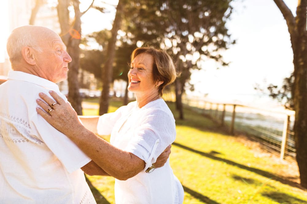 Charter Senior Living of Cleveland Residents couple dressed all in white smiles and dances together outdoors 